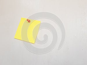 Yellow sticky note pinned to a white wall with red push pin