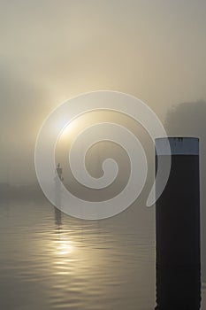 Bright yellow sun in the day mist and its reflexion in the calm river