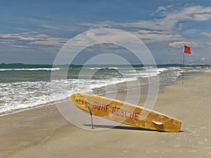 Bright yellow surfboard in the form of pointer with a red words rescue on a sandy beach