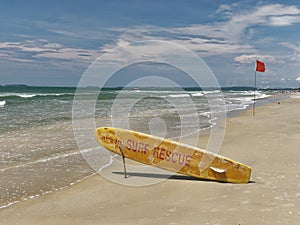Bright yellow surfboard in the form of pointer with a red words rescue on a sandy beach