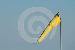 A bright yellow windsock against a clear blue sky.