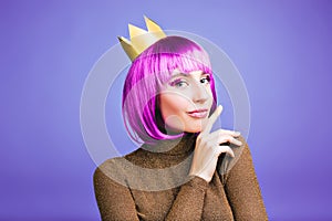 Brightful stylish portrait of charming young woman in gold crown, short purple hair on violet background. Celebrating