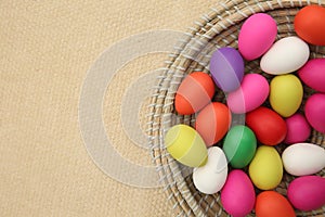 Brightly colored easter eggs, in a straw basket against a beige background