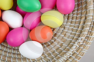 Brightly coloured easter eggs, in a straw basket against a grey background