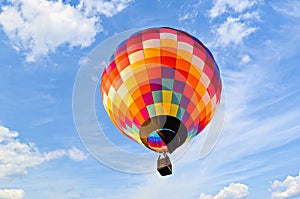 Brightly colored hot air balloon soaring through a bright blue sky, with clouds in the background