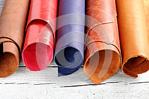 Brightly colored leather in rolls on the wooden background. Leather craft.