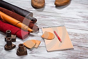 Brightly colored leather in rolls, working tools, shoe lasts, notebook with pencil on white background. Leather craft.