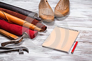Brightly colored leather in rolls, working tools, shoe lasts, notebook with pencil on white background. Leather craft.