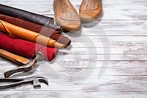 Brightly colored leather in rolls, working tools and shoe lasts on white wooden background. Leather craft. Copy space.