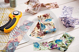 Brightly colored strips of fabric, rotary cutter and quilting accessories on white wooden surface