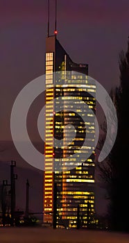 Brightly illuminated skyscraper with a dazzlingly lit top stands tall in the foreground