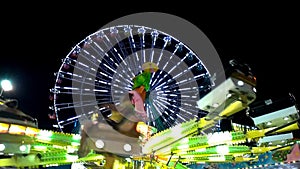 Brightly lit ferris wheel ride spinning at night at a carnival, amusement park, theme park, fair, thrill park.