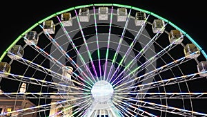 Brightly lit ferris wheel ride spinning at night at a carnival, amusement park, theme park, fair, thrill park.