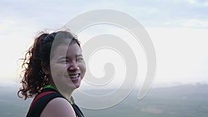 Brightly lit portrait of cheerful girl on top of mountain with beautiful view background in early morning