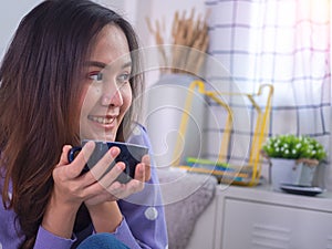 Brightly smiling Asian women enjoyed drink coffee in the morning. Woman holding a coffee cup and looking out the window in the bed