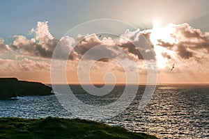 Brilliant blazing sun sets along rugged coast of Ireland`s Loop Head Peninsula, County Clare, Ireland. Seabirds circle overhead.