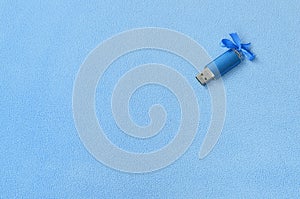 Brilliant blue usb flash memory card with a blue bow lies on a blanket of soft and furry light blue fleece fabric. Classic female