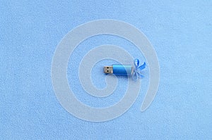 Brilliant blue usb flash memory card with a blue bow lies on a blanket of soft and furry light blue fleece fabric. Classic female