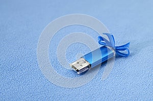 Brilliant blue usb flash memory card with a blue bow lies on a blanket of soft and furry light blue fleece fabric. Classic female