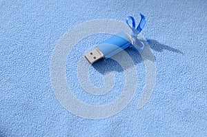 Brilliant blue usb flash memory card with a blue bow lies on a blanket of soft and furry light blue fleece fabric. Classic female