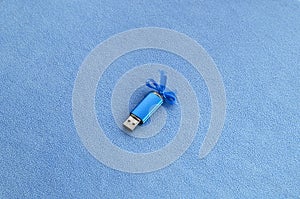 Brilliant blue usb flash memory card with a blue bow lies on a blanket of soft and furry light blue fleece fabric. Classic female