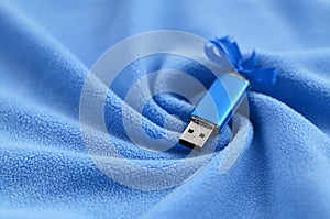 Brilliant blue usb flash memory card with a blue bow lies on a blanket of soft and furry light blue fleece fabric with a lot of re