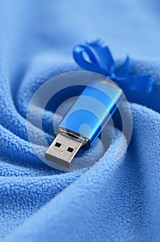 Brilliant blue usb flash memory card with a blue bow lies on a blanket of soft and furry light blue fleece fabric with a lot of re