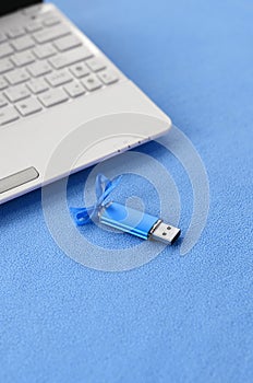 Brilliant blue usb flash memory card with a blue bow lies on a blanket of soft and furry light blue fleece fabric beside to a whit