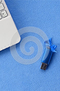 Brilliant blue usb flash memory card with a blue bow lies on a blanket of soft and furry light blue fleece fabric beside to a whit