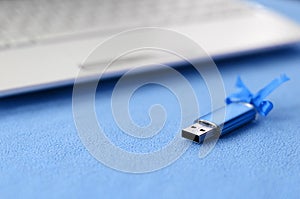 Brilliant blue usb flash memory card with a blue bow lies on a blanket of soft and furry light blue fleece fabric beside to a whit