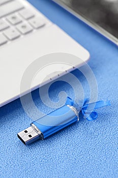 Brilliant blue usb flash memory card with a blue bow lies on a blanket of soft and furry light blue fleece fabric beside to a whit