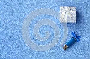 Brilliant blue usb memory card with a blue bow lies next to a small gift box in blue with a small bow on a blanket of soft and fur