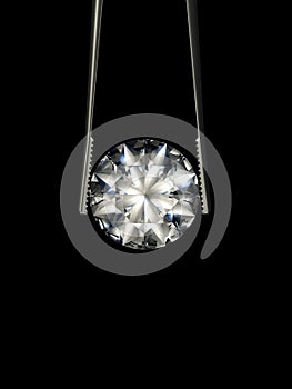 Brilliant cut diamond held by tweezers on a black background. Beautiful sparkling shining round shape.