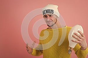 Brilliant idea. Genius idea. Portrait of young man having idea over pink background. Guy in hat holds lamp in hand. Idea