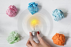 Brilliant and original idea suggested by glowing light bulb in womanâ€™s hand and crumpled paper against white background