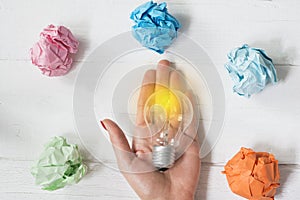 Brilliant and original idea suggested by glowing light bulb in womanâ€™s hand and crumpled paper against white background