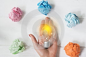 Brilliant and original idea suggested by glowing light bulb in womanâ€™s hand and crumpled paper against white background