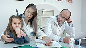 Bring your daughter to work day. Mother nurse talking to her little girl while sitting in the office with male coworker.