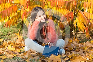 Bringing school into nature. Cute primary school child with book sit on yellow leaves. Happy little girl back to school