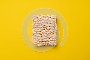 Briquette of instant dry egg noodles on yellow background