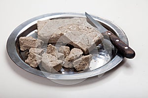 Briquettes and pieces of sunflower halva and a knife lie on a metal grater on a white background