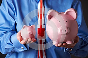 British Businessman Holding Large And Small Piggy Bank