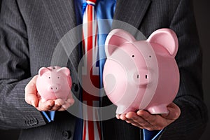 British Businessman Holding Large And Small Piggy Bank