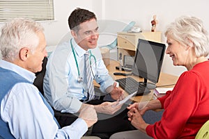 British GP talking to senior couple in surgery