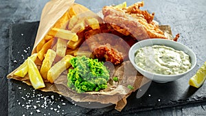 British Traditional Fish and chips with mashed peas, tartar sauce on crumpled paper.