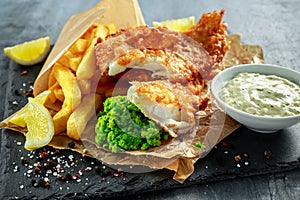 British Traditional Fish and chips with mashed peas, tartar sauce on crumpled paper.