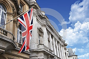 British Union Jack flag on a pole with buildings and a beautiful cloudy blue sky