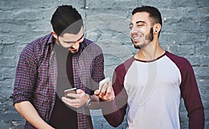 Bro, look who wants to chat. two young men standing outdoors and using a mobile phone against a gray wall.