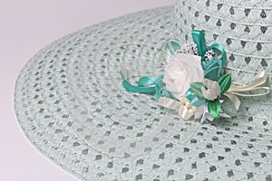 A broad-brimmed female hat is light green, with a buttonhole. Artificial flowers in the form of roses.