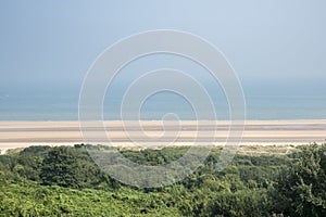 A broad, sandy beach on a bright summers day. The coastline is Normandy, in North